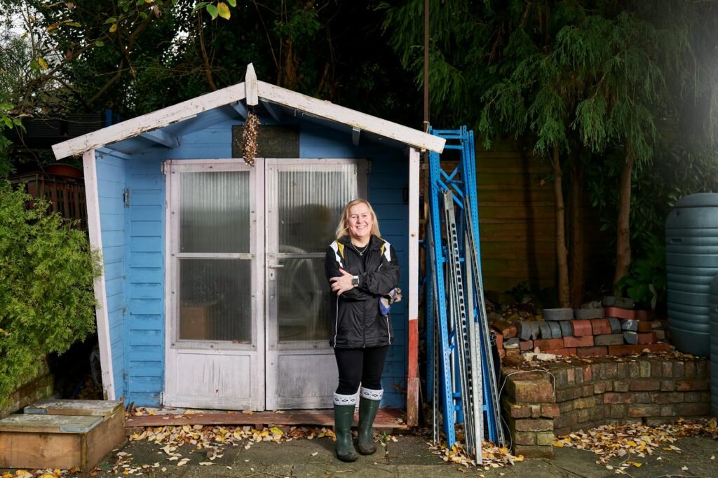 a woman in blue jacket standing in front of a blue shed