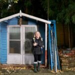 a woman in blue jacket standing in front of a blue shed