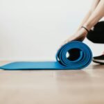 crop young sportswoman unfolding blue fitness mat